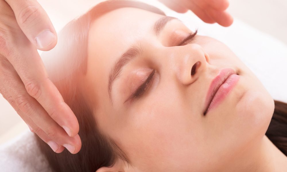Close-up Of Therapist's Hand Performing Reiki Treatment On Young Woman In Spa